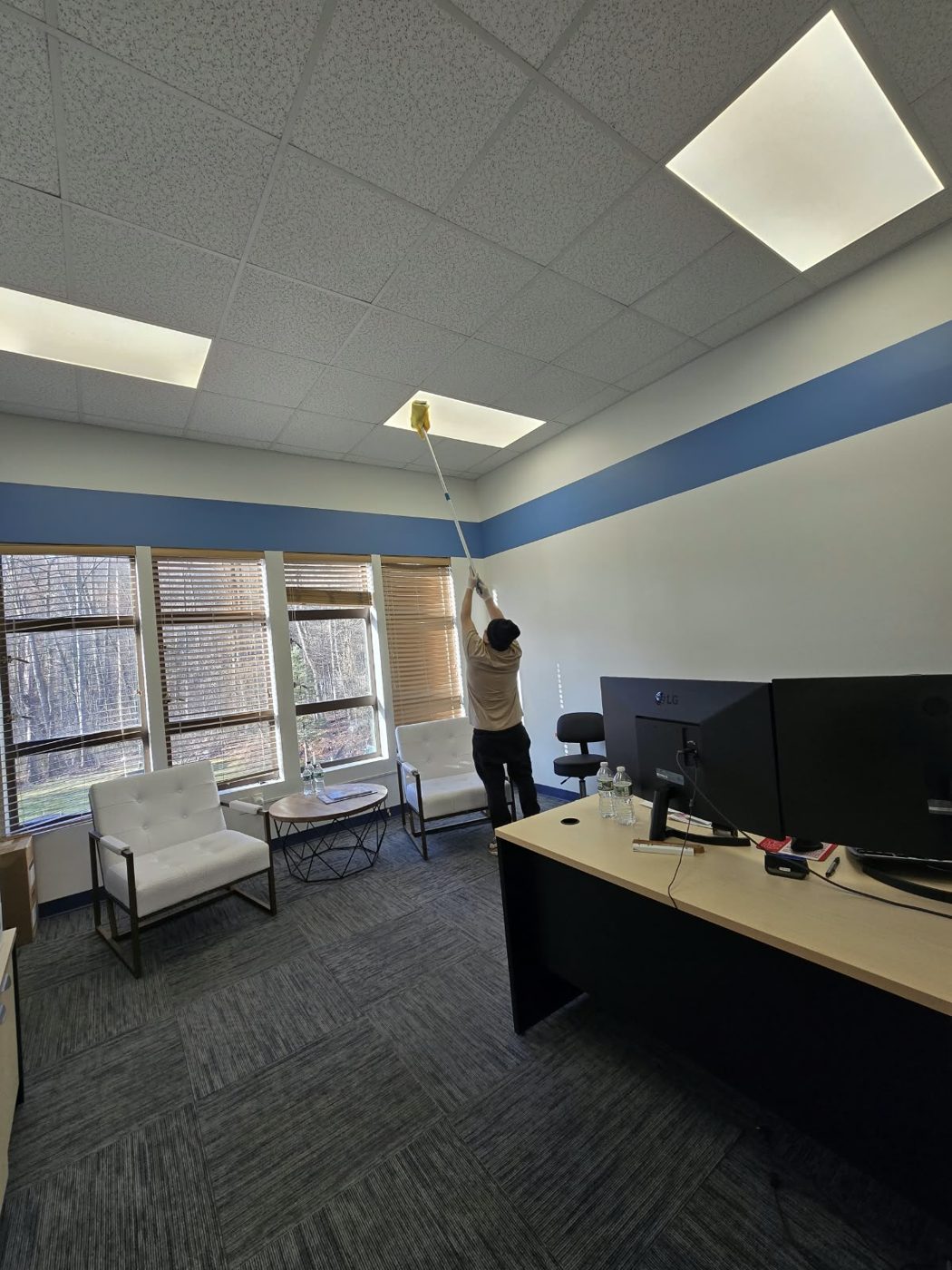 Fine Cleaning team member dusting ceiling light panels with an extension duster